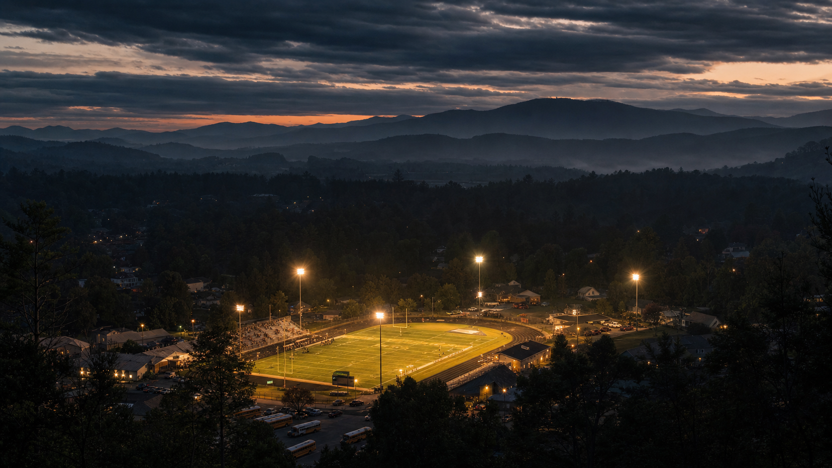 Aerial dusk view of a small-town Carolina high school stadium under the lights.