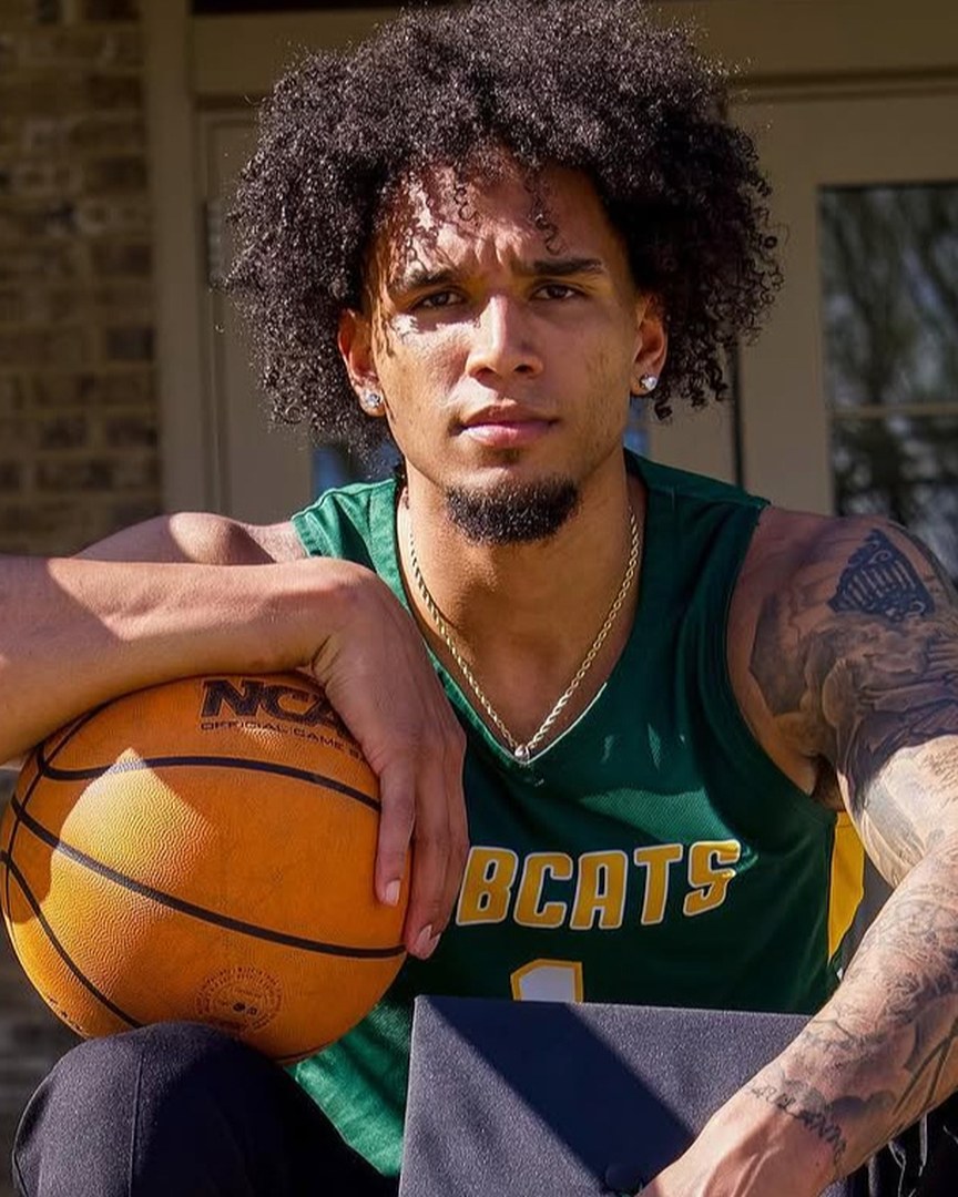 Portrait of Sidney Dollar in his green Lees-McRae Bobcats basketball jersey, resting a hand on a basketball beside his graduation cap.
